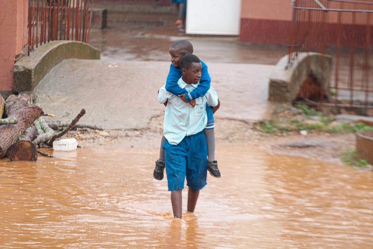 A man carries a child through a flooded city street during heavy rain, showcasing resilience.